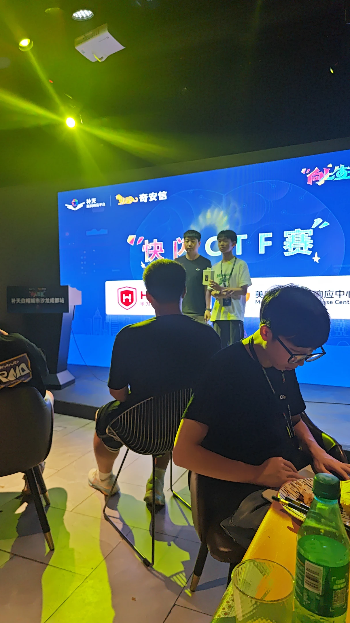 快闪CTF现场,队员在电脑前操作,身后是舞台和参赛者