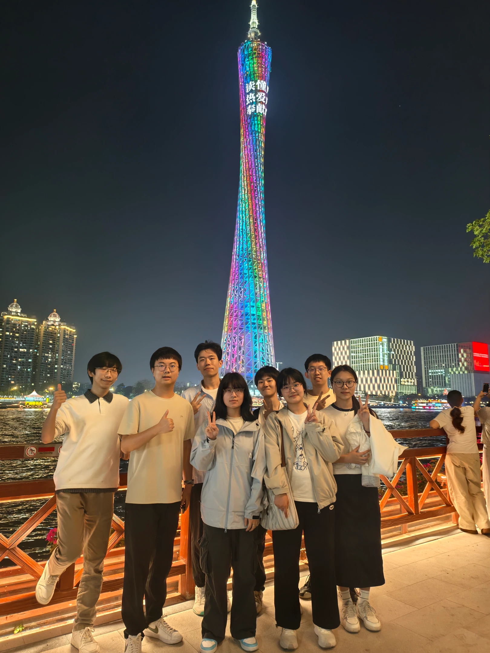 队员们站在江边栏杆前合影,身后是亮起彩色灯光的高塔